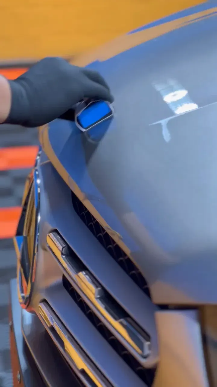Mão com luva preta aplicando a vitrificação com aplicador sobre a pintura de um carro